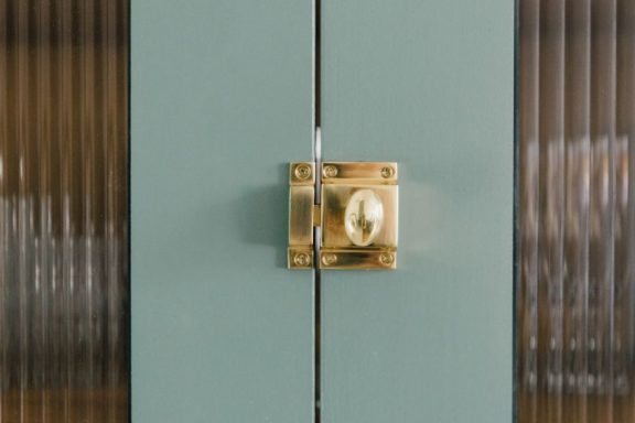 A kitchen wall cabinet with fluted glass fitted with a brass latch, painted in farrow and ball Breakfast room green paint.
